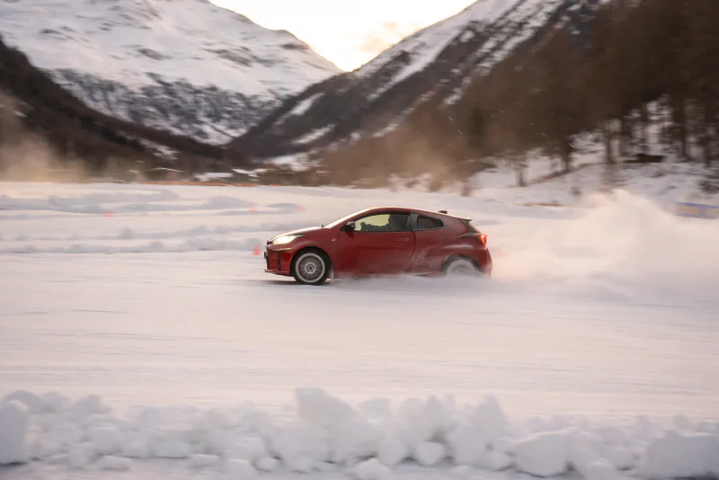 Rotes Auto driftet über die Eisstrecke vor verschneiten Bergen