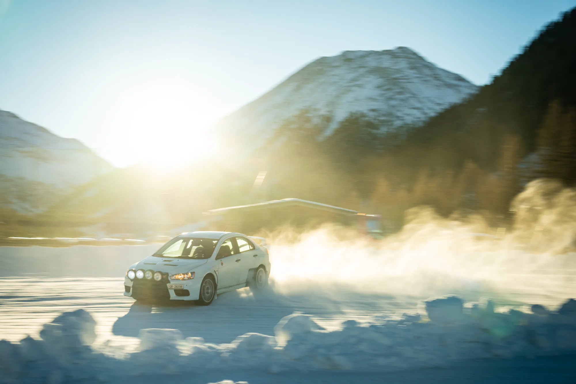 Mitsubishi Evo driftet im Gegenlicht über die verschneite Eisstrecke im Engadin