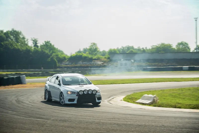 Weisser Mitsubishi Lancer Evolution driftet mit Rauch durch eine Kurve