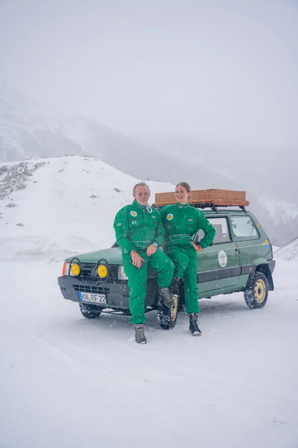 Zwei Fahrer in grünen Overalls vor ihrem Fiat Panda im Schnee